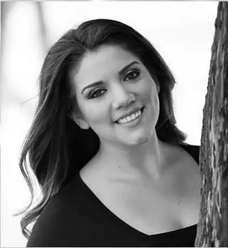 Smiling person leaning against tree, black and white photo.