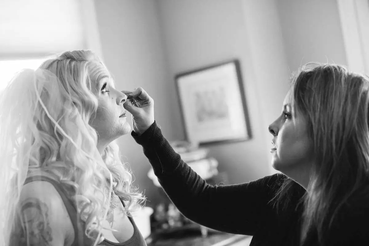 A professional makeup artist applies concealer to a bride on her wedding day.